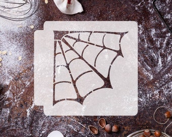 May include: A white plastic stencil with a spiderweb design. The stencil is on a brown surface with flour scattered around it.