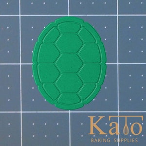 May include: Green plastic turtle shell cookie cutter. The shell has a hexagonal pattern.