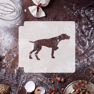 Può includere: Uno stencil bianco con la silhouette di un cane marrone su una superficie marrone rustica con farina e altri ingredienti da forno.