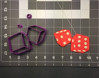 Puede incluir: Dos dados rojos con puntos blancos y dos cortadores de galletas de plástico morado en forma de dados.