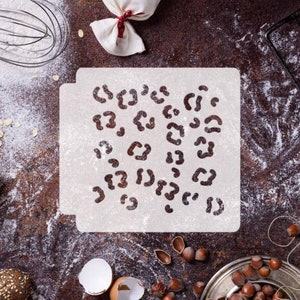 Może przedstawiać: Biała plastikowa szablon z wzorem lamparta. Szablon znajduje się na brązowej powierzchni z rozsypaną mąką.