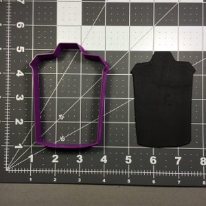 Może przedstawiać: Fioletowa plastikowa foremka do ciasteczek w kształcie kosza na śmieci. Foremka do ciasteczek znajduje się na czarno-białym tle siatki.