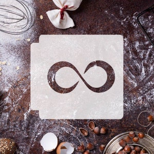May include: A white stencil with an infinity symbol cut out. The stencil is on a brown surface with flour scattered around it.
