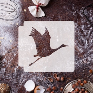 May include: White stencil featuring a silhouette of a crane in flight. The stencil is on a brown surface with flour scattered around it.
