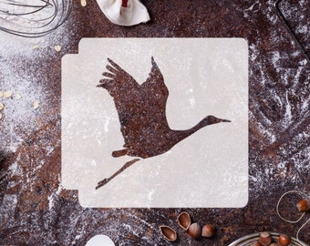 May include: White stencil with a silhouette of a crane in flight. The stencil is on a brown surface with flour scattered around it.