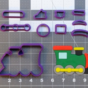 Puede incluir: Cortadores de galletas de plástico morado en forma de locomotora, vagón, ruedas, un círculo, un cuadrado, una nube, un rectángulo, una luna creciente y un rectángulo pequeño. También hay un cortador de galletas de plástico verde y rojo en forma de locomotora.