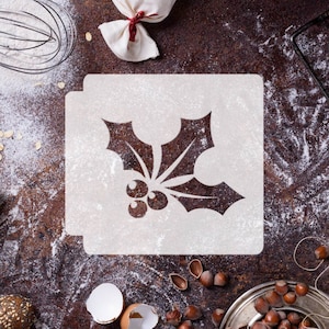 Puede incluir: Plantilla blanca de una hoja de acebo con bayas sobre una superficie marrón con harina y otros suministros de repostería.