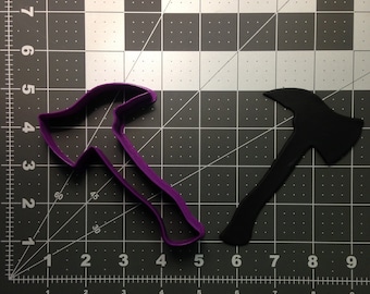 May include: Two axe-shaped cookie cutters, one purple and one black, on a grey gridded surface.