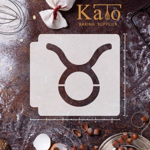 May include: White plastic stencil of the Taurus zodiac sign with a ruler marked in inches. The stencil is on a brown surface with flour and hazelnuts.