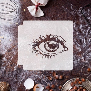 May include: White stencil featuring a black eye design. The stencil is on a brown surface with flour scattered around it.