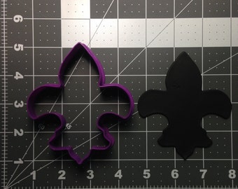 Könnte beinhalten: Lilafarbener Plastik-Ausstecher in Form einer Fleur-de-lis. Der Ausstecher befindet sich auf einem schwarz-weißen Gitterhintergrund.