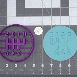 Könnte beinhalten: Zwei runde, 3D-gedruckte Ausstecher in Form eines Schaltmusters eines Autos. Der Ausstecher links ist lila und der Ausstecher rechts ist blau.