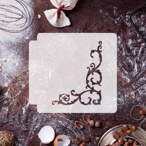 May include: A white stencil with a decorative corner design. The stencil is on a brown surface with flour scattered around it.