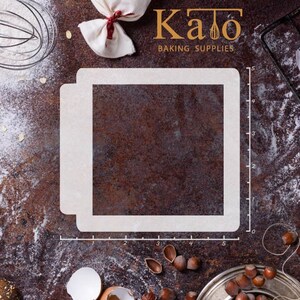 May include: A white plastic stencil for baking, measuring 12.7 cm by 12.7 cm. The stencil is on a brown, textured surface with a ruler marked in centimetres.