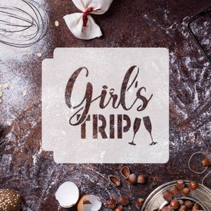 Op de afbeelding: Witte sjabloon met de tekst "Girl's Trip" en twee champagne glazen. De sjabloon ligt op een bruin oppervlak met verspreid meel.