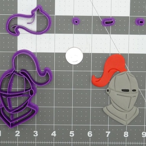 May include: A collection of purple plastic cookie cutters in the shape of knight helmets and helmet parts. One complete helmet is gray with a red plume. The cutters are arranged on a gray grid.