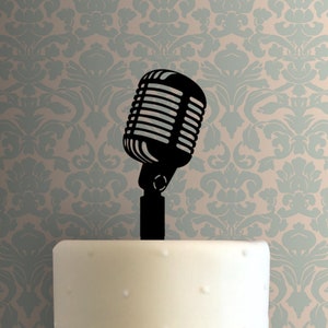 May include: Black silhouette of a vintage microphone on a white cake. The microphone has a round head with a grill and a long, thin stand.