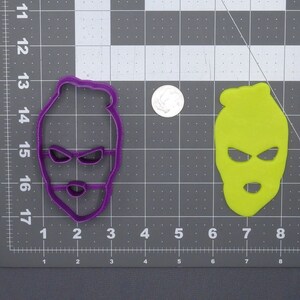 May include: Two plastic cookie cutters shaped like a ski mask, one purple and one green.