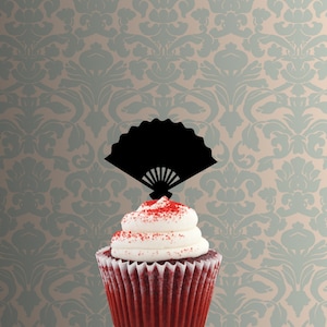 以下が含まれることがあります： 赤いベルベットのカップケーキに白いフロスティングと赤いスプリンクルがトッピングされ、黒い紙の扇形のカップケーキトッパーが飾られています
