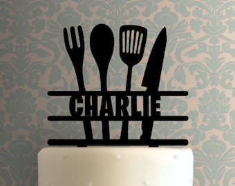 May include: Black silhouette cake topper featuring a fork, spoon, spatula, and knife, with the name "CHARLIE" in the centre.