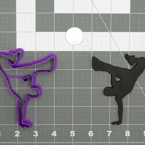 May include: Purple and black cookie cutters shaped like a person breakdancing. The cookie cutters are on a gray grid background.