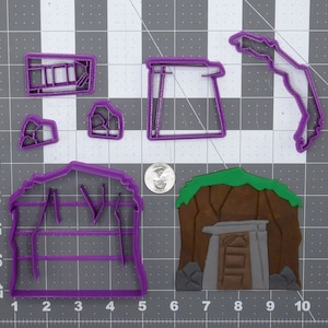 May include: Purple plastic cookie cutters in the shape of a mine, a mine cart, a pickaxe, a lantern, and a rock. The cutters are on a gray grid background.