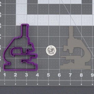 Puede incluir: Cortador de galletas de plástico morado con forma de microscopio. El cortador de galletas está sobre un fondo de rejilla gris.