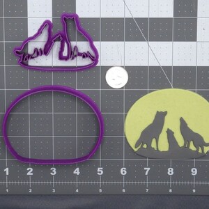 Puede incluir: Tres cortadores de galletas de lobo, uno con luna llena, otro con tres lobos aullando a la luna y otro con tres lobos de pie juntos.