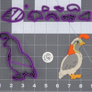 May include: Purple plastic cookie cutters in the shape of a quail, a wing, a tail, and other shapes. The cutters are on a gray grid background.