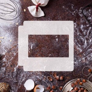 Könnte beinhalten: Draufsicht auf Backzutaten und -werkzeuge auf einer rustikalen braunen Oberfläche. Enthält eine weiße rechteckige Schablone, Mehl, einen Schneebesen, einen kleinen Beutel mit roter Schleife und einen Teller mit Haselnüssen. Backthema.