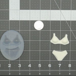 May include: A white silicone mold for making a cake or other dessert. The mold is shaped like a face with a smiling expression. There is also a mold for a bra and a pair of underwear.