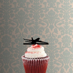 May include: Red velvet cupcake with white frosting and red sprinkles topped with a black airplane silhouette cake topper.