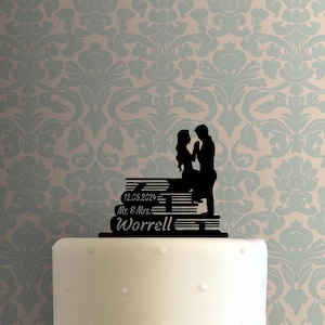 Puede incluir: Topper de pastel en silueta negra de una pareja de pie sobre una pila de libros. Los libros tienen el texto "12.05.2024 Mr. & Mrs. Worrell".