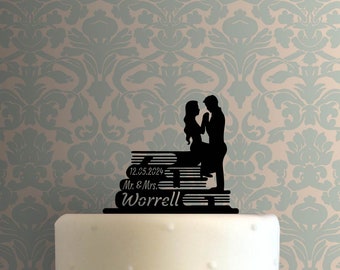May include: Black silhouette cake topper of a couple standing on a stack of books. The books have the text "12.05.2024 Mr. & Mrs. Worrell" on them.