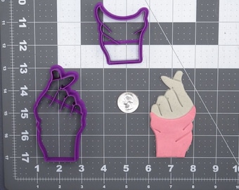 May include: Two purple plastic cookie cutters shaped like hands making the Korean heart sign. One cutter is a flat design and the other is a more detailed design.