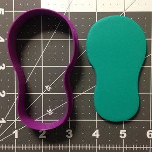 May include: Purple plastic cookie cutter shaped like a lightbulb, next to a green fondant lightbulb cutout.
