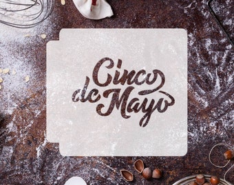 May include: A white stencil with the text "Cinco de Mayo" in a decorative font. The stencil is on a brown surface with flour scattered around it.