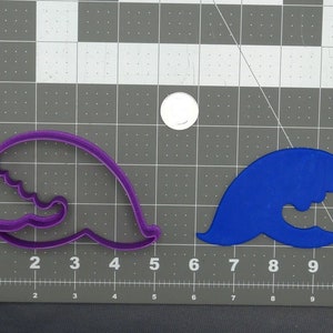 May include: Two cookie cutters, one purple and one blue, shaped like a wave. The cutters are on a grey grid surface.
