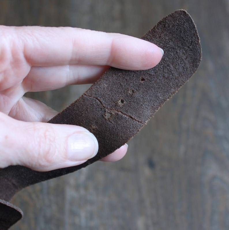 May include: A close-up of a brown leather strap with multiple holes punched in it. The strap is slightly worn and has a few creases.