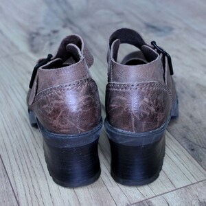 May include: A pair of brown leather heeled sandals with buckles. The sandals have a textured leather upper and a chunky heel.