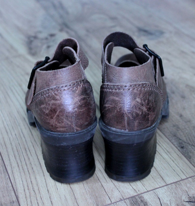 May include: A pair of brown leather heeled sandals with buckles. The sandals have a textured leather upper and a chunky heel.