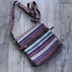 May include: A striped crochet crossbody bag with a brown leather strap. The bag has a zipper closure and a multi-colored striped pattern.