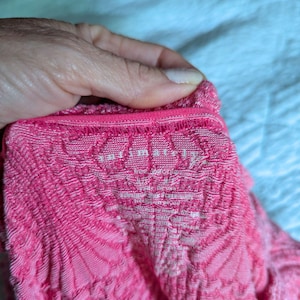 May include: Close-up of a pink, textured fabric with a repeating pattern. The fabric has a scalloped edge and the text "Intimately Free People" is visible. The fabric appears to be a knit or crochet material.
