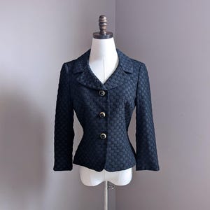 May include: A black blazer with a textured woven fabric and gold buttons. The blazer has a fitted silhouette and a collar.
