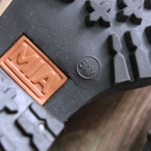 May include: Close-up of the bottom of a black shoe with a brown leather label that says "MIA" and a black circle with the text "41/2 1/3" inside.