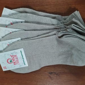 May include: A stack of six pairs of gray ankle socks with a mesh pattern. The socks have a blue trim and a red and white label that says "Nova Liniya" with the website address printed below.