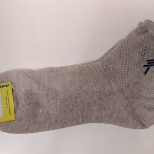 May include: A single light gray sock with a mesh design and a small blue and black embroidered detail. A yellow tag with Ukrainian text is attached to the sock. The sock is made of natural materials.