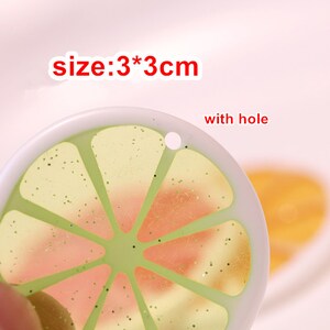 May include: A green and pink lemon slice shaped resin charm with glitter. The charm is 3 inches in diameter and has a hole for hanging.  The text "size: 3*3cm" is visible in the image.
