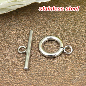 May include: A silver-colored stainless steel toggle clasp consisting of a T-bar component with a small attached loop and a circular ring component with a small attached loop. The text stainless steel is visible in the upper portion of the image.