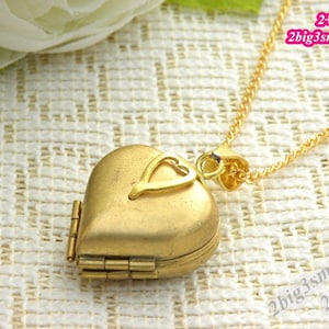 Peut inclure: Un collier avec un pendentif en forme de cœur en or, orné d'un petit cœur. Le pendentif s'ouvre par une charnière et est attaché à une chaîne en or.